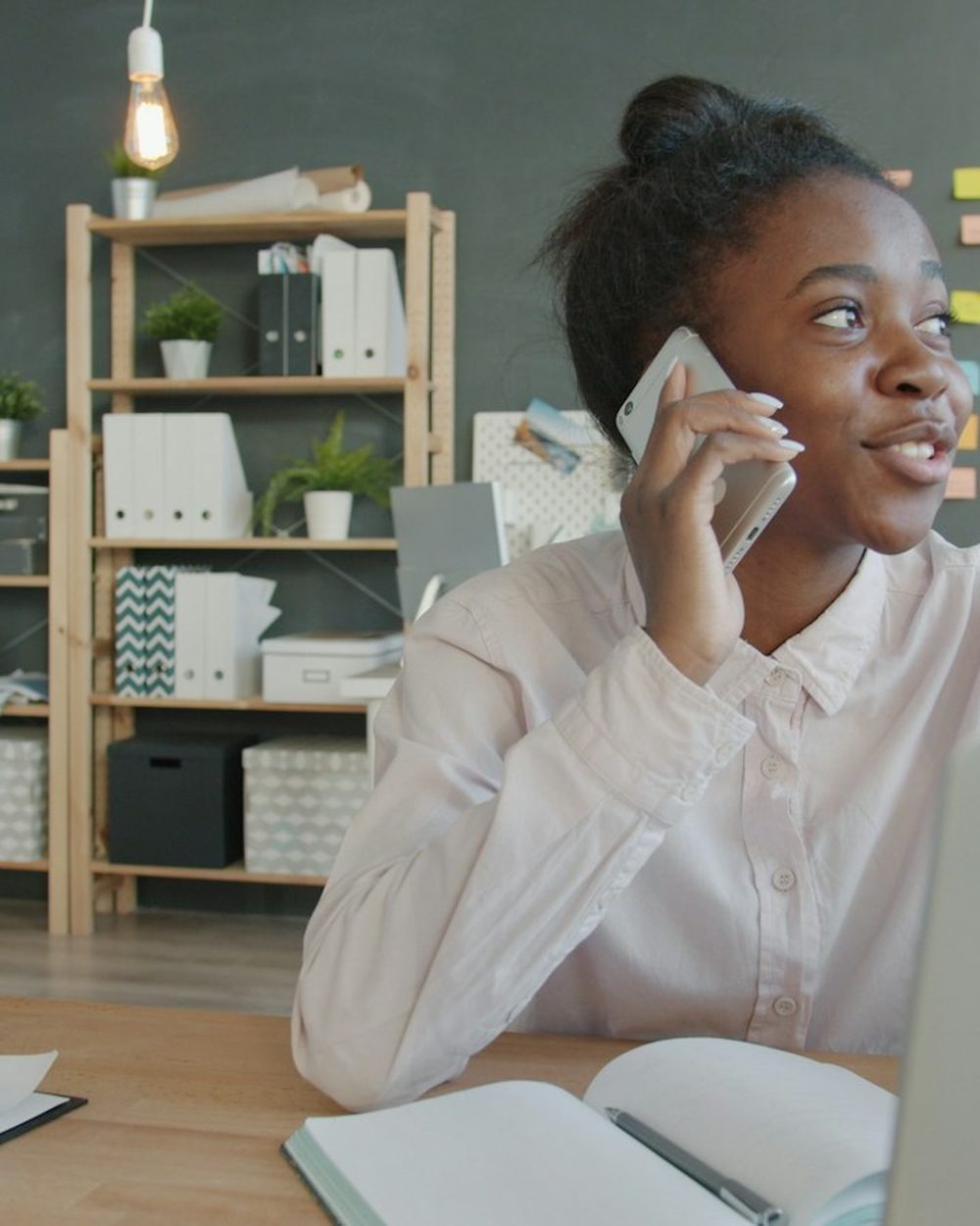 A smiling young woman on a phone call at her desk