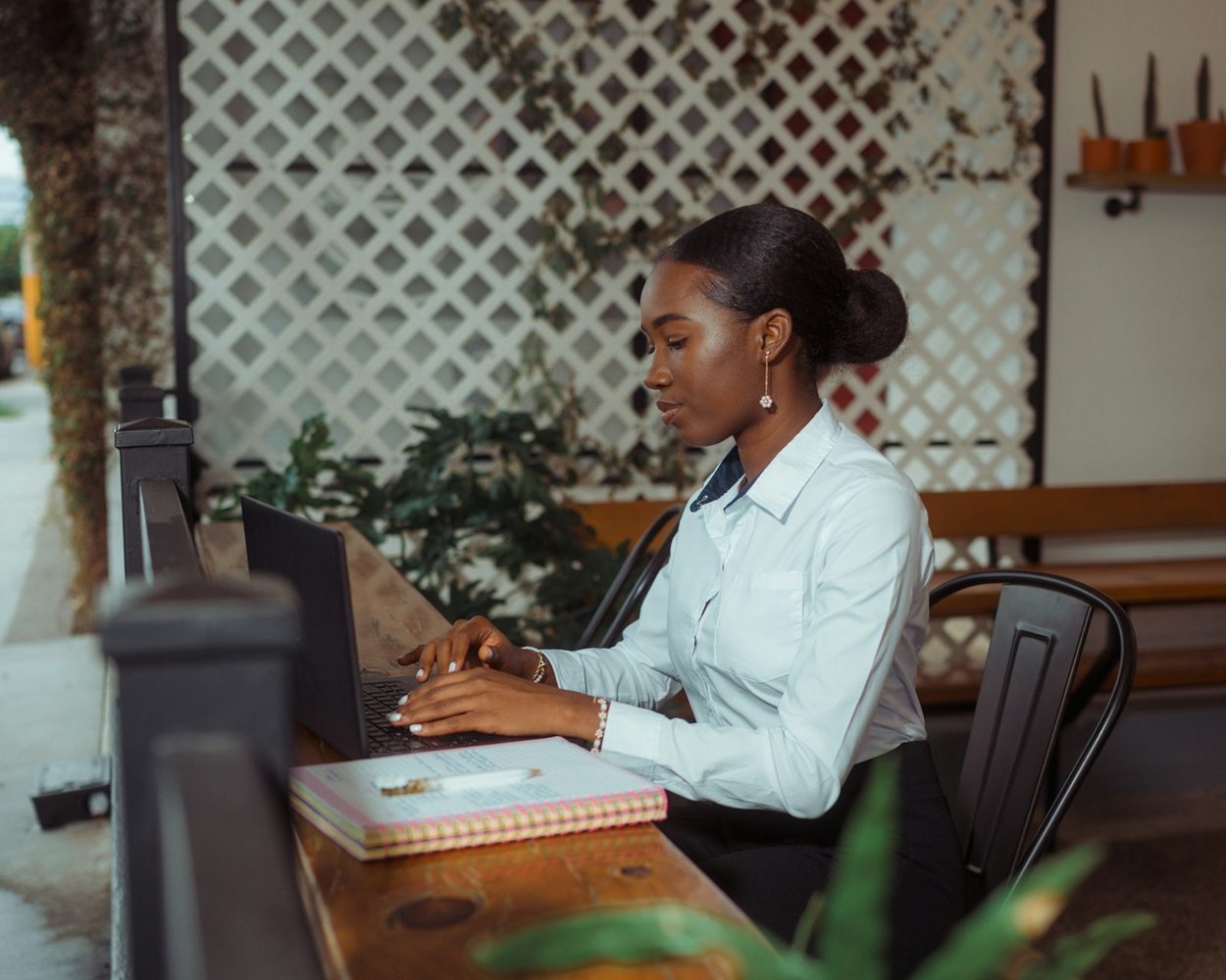 A professional working on a laptop at a table on a shaded terrace